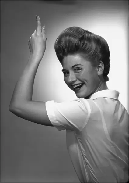 Woman pointing up in studio, (B&W), portrait