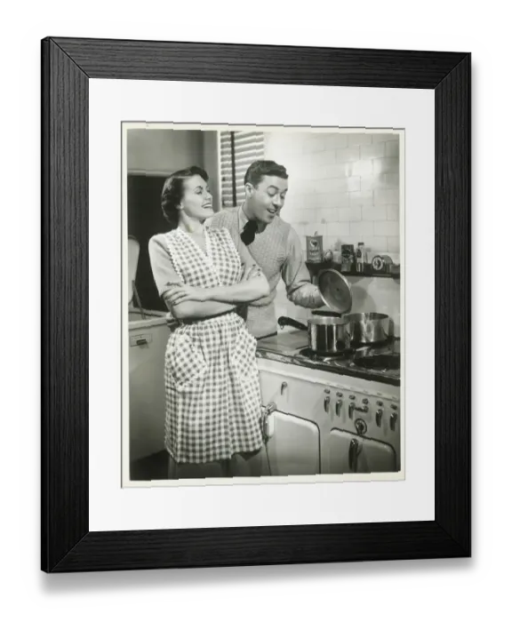 Framed Print : Man looking into pot in domestic kitchen, woman smiling Framed Print : Man looking into pot in domestic kitchen, woman smiling