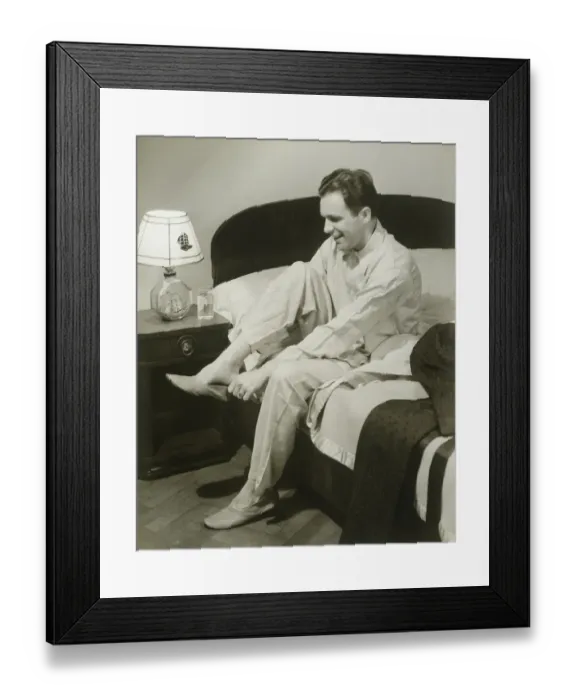 Framed Print : Mature man sitting on bed putting on slippers, smiling Framed Print : Mature man sitting on bed putting on slippers, smiling
