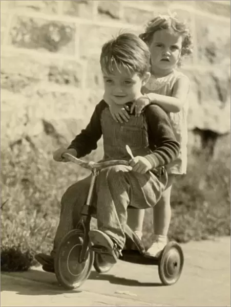 Little boy giving little girl ride on tricycle
