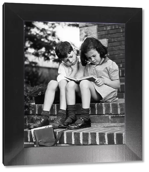 Young boy & girl reading a book outdoors
