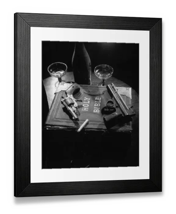Framed Print : Holy Gun Smoke; Two hand guns and a cigarette lying on a copy of the Holy Bible in a production of Edgar Wallaces play On The Spot
