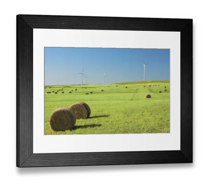 Framed Print : Hay bales in a green field with wind turbines against a blue sky