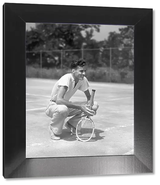 Young Man Smiling Squatting Holds Tennis Racquet A