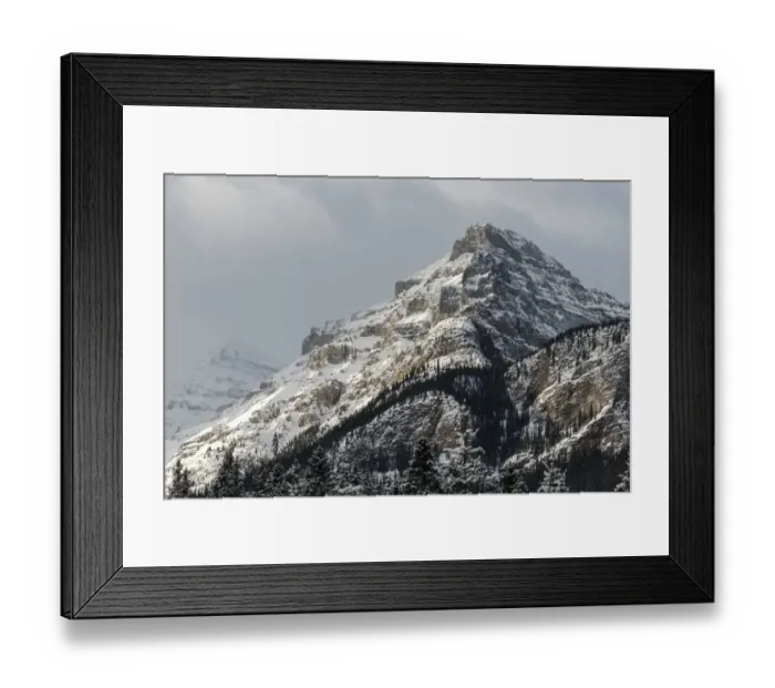 Framed Print : Rugged mountain peak with snow under a cloudy sky