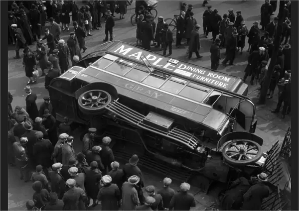 Bus Crash. circa 1925: A crowd of passers-by gather round an overturned