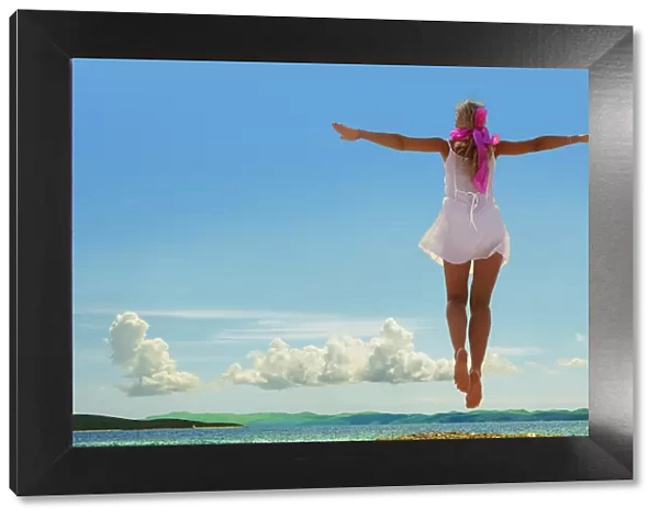 Woman jumping on beach, arms outstretched, rear view