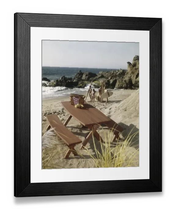 Framed Print : Picnic table with surfers on beach in background Framed Print : Picnic table with surfers on beach in background