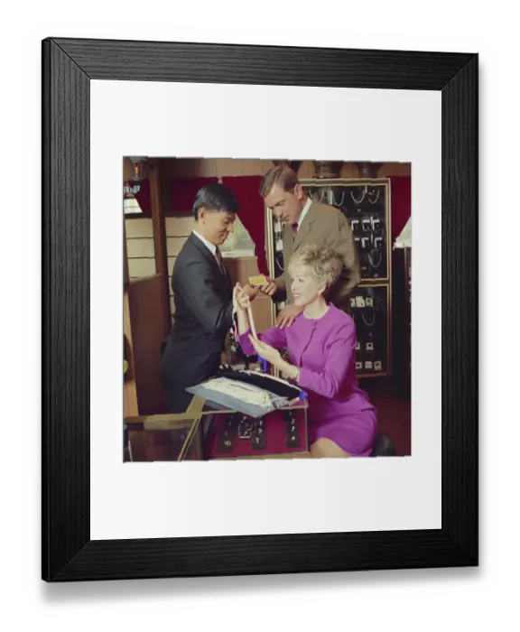 Framed Print : Men and woman sitting at table in jewellery shop and looking at pearl necklaces