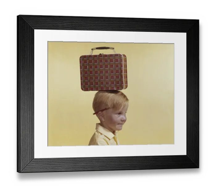 Framed Print : Boy with small luggage on his head against yellow background, close-up Framed Print : Boy with small luggage on his head against yellow background, close-up