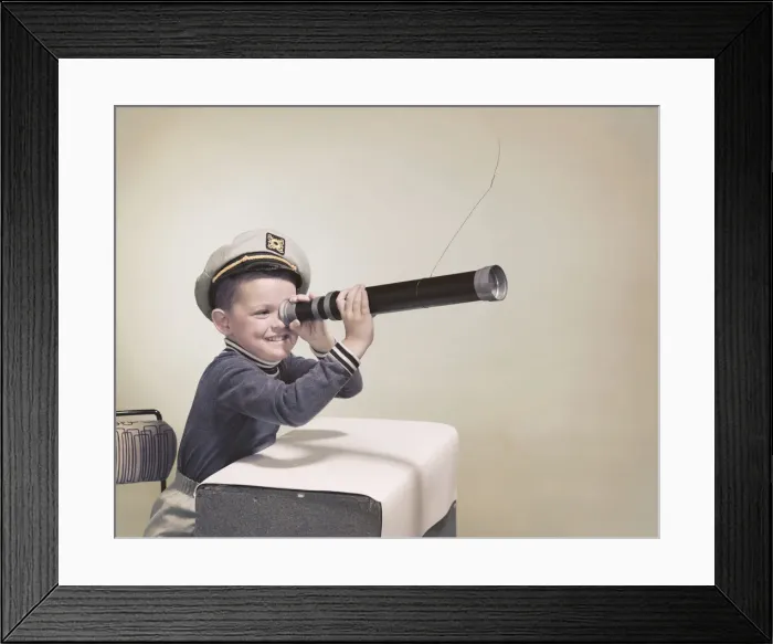 Framed Print : Boy wearing sailor hat looking through telescope, smiling Framed Print : Boy wearing sailor hat looking through telescope, smiling