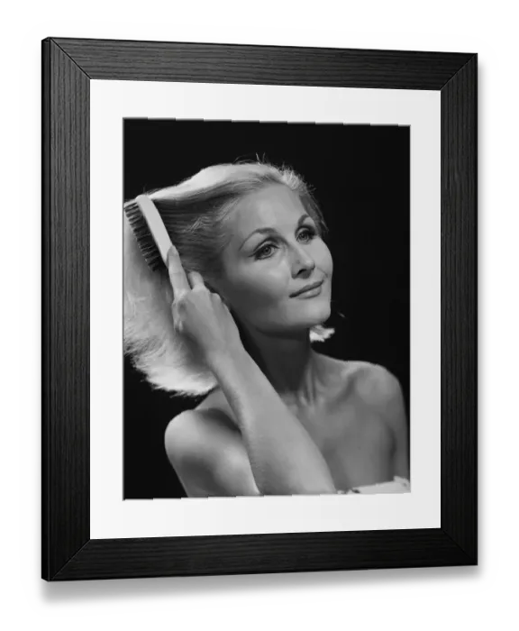 Framed Print : Woman combing hair against black background, close-up