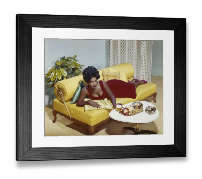 Framed Print : Young woman lying on sofa with snacks on table, portrait Framed Print : Young woman lying on sofa with snacks on table, portrait