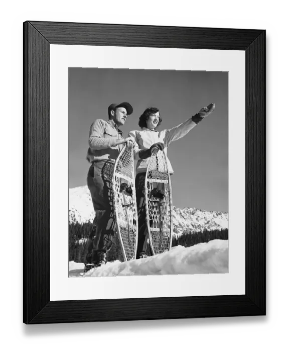 Framed Print : Couple holding snowshoes, woman pointing Framed Print : Couple holding snowshoes, woman pointing