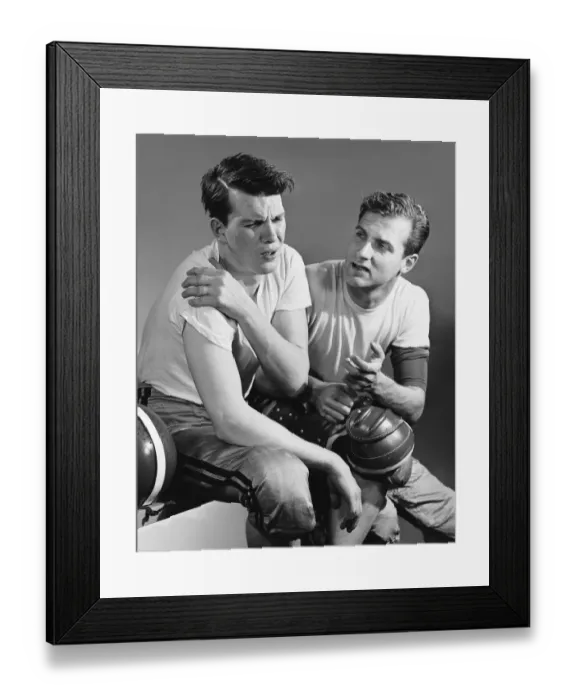 Framed Print : Football player holding sore shoulder; trainer sitting beside him Framed Print : Football player holding sore shoulder; trainer sitting beside him