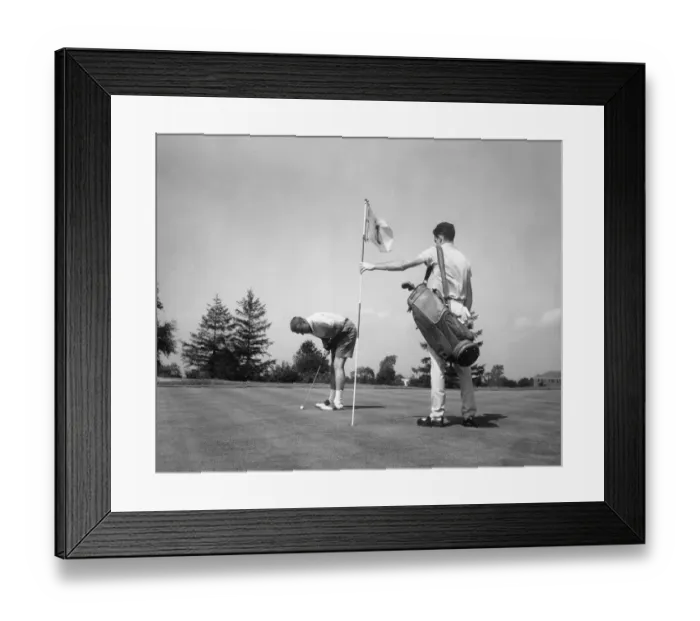 Framed Print : Man making golf shot while caddie stands holding flag Framed Print : Man making golf shot while caddie stands holding flag
