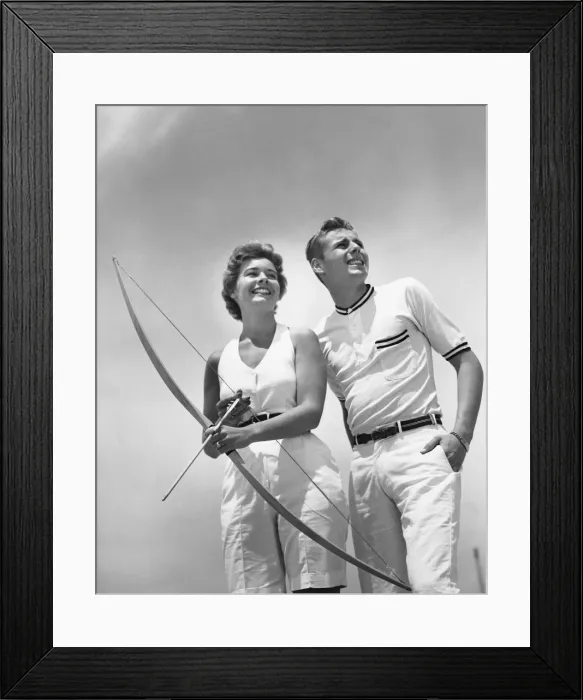 Framed Print : Man standing beside woman who is holding bow and arrow Framed Print : Man standing beside woman who is holding bow and arrow