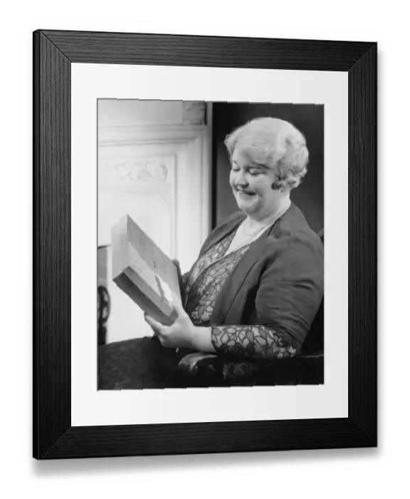 Framed Print : Mature woman holding gift in living room, (B&W) Framed Print : Mature woman holding gift in living room, (B&W)