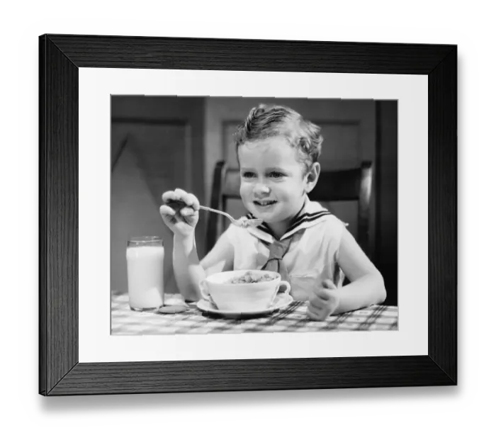 Framed Print : Boy (4-5) wearing sailor suit, eating at table, (B&W), portrait