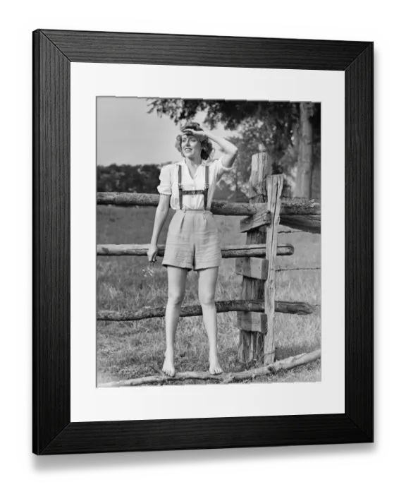 Framed Print : Barefoot woman in shorts standing on wooden fence on meadow, (B&W) Framed Print : Barefoot woman in shorts standing on wooden fence on meadow, (B&W)