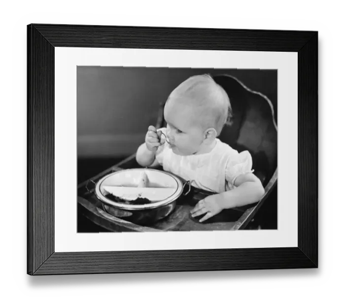 Framed Print : Baby girl (6-12 months) in high chair eating, (B&W), close-up Framed Print : Baby girl (6-12 months) in high chair eating, (B&W), close-up