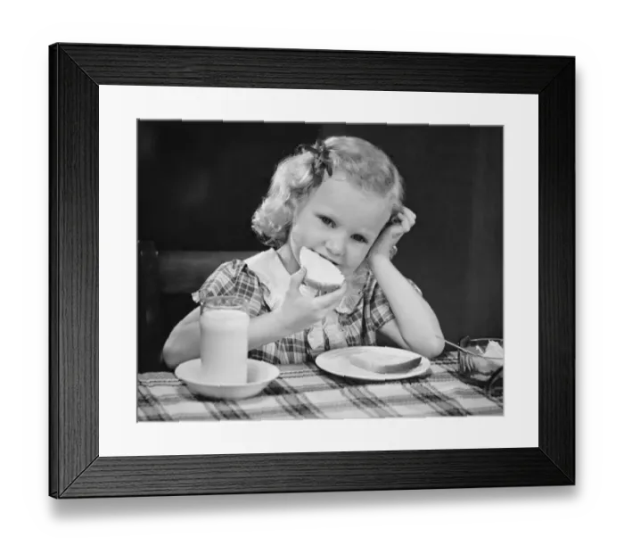 Framed Print : Girl (6-7) eating breakfast, resting head on hand, (B&W)
