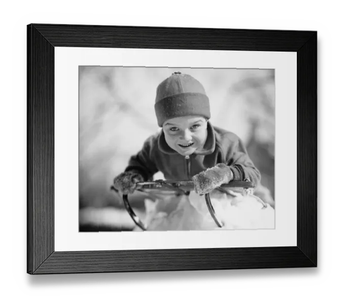 Framed Print : Boy (6-7) lying on sled in snow, (B&W), portrait Framed Print : Boy (6-7) lying on sled in snow, (B&W), portrait