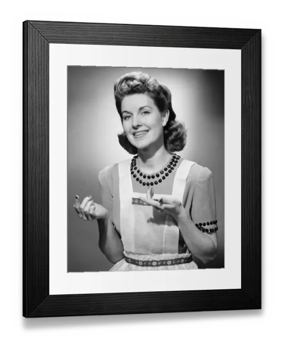 Framed Print : Young woman wearing apron, standing, smiling, (B&W) Framed Print : Young woman wearing apron, standing, smiling, (B&W)
