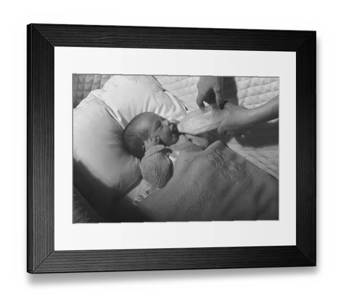 Framed Print : Mother feeding baby (0-3 months) lying in crib with baby bottle, (B&W), close-up Framed Print : Mother feeding baby (0-3 months) lying in crib with baby bottle, (B&W), close-up