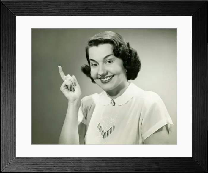 Framed Print : Smiling woman pointing finger in studio, (B&W), (Close-up), (Portrait)
