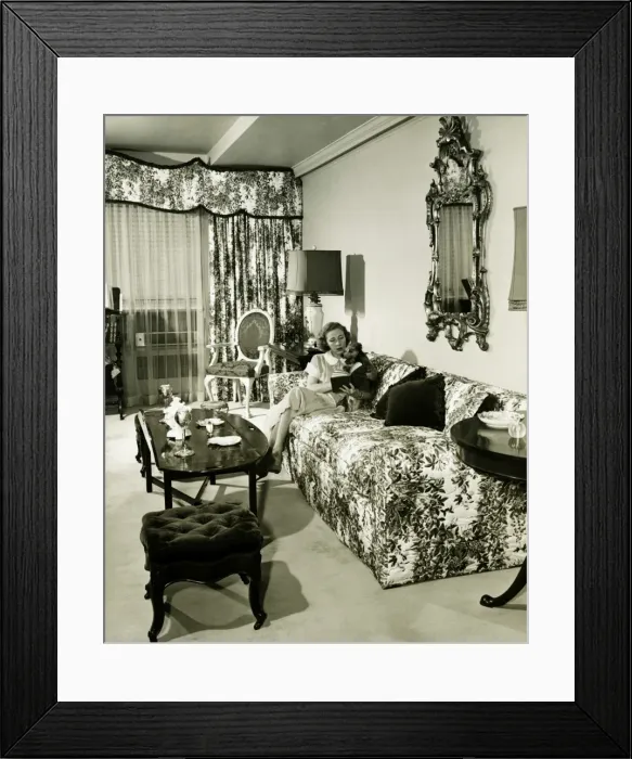 Framed Print : Woman sitting on couch in opulent living room, reading book, (B&W) Framed Print : Woman sitting on couch in opulent living room, reading book, (B&W)