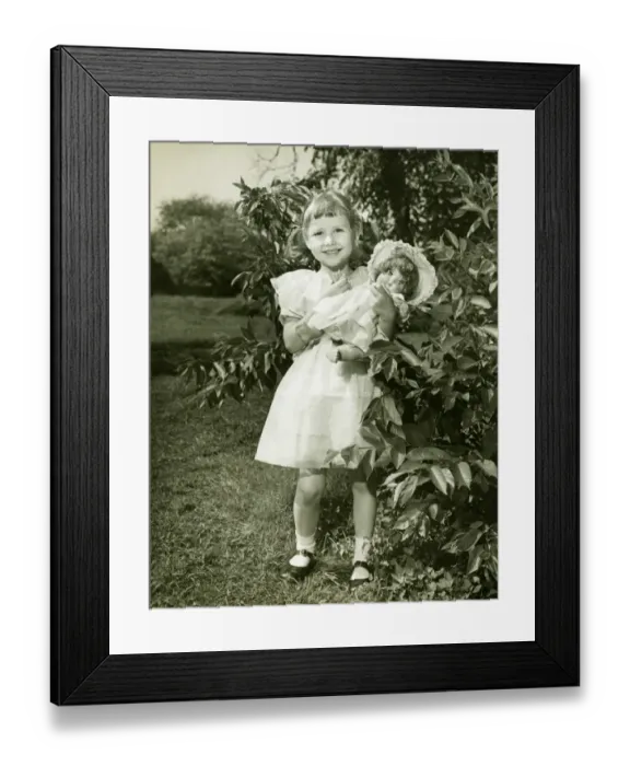 Framed Print : Girl (6-7) holding doll, posing in park, (B&W), (Portrait) Framed Print : Girl (6-7) holding doll, posing in park, (B&W), (Portrait)