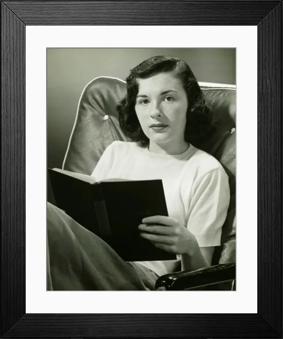 Framed Print : Woman sitting on armchair, holding book, (B&W), (Portrait) Framed Print : Woman sitting on armchair, holding book, (B&W), (Portrait)