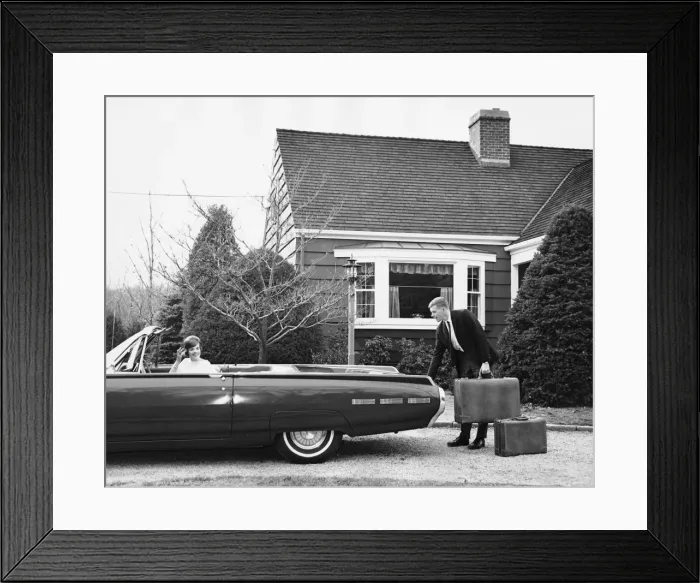 Framed Print : Man loading trunk with suitcases while woman waits in car