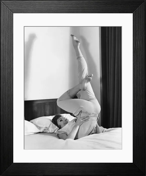 Framed Print : Woman lying on bed, doing exercises Framed Print : Woman lying on bed, doing exercises
