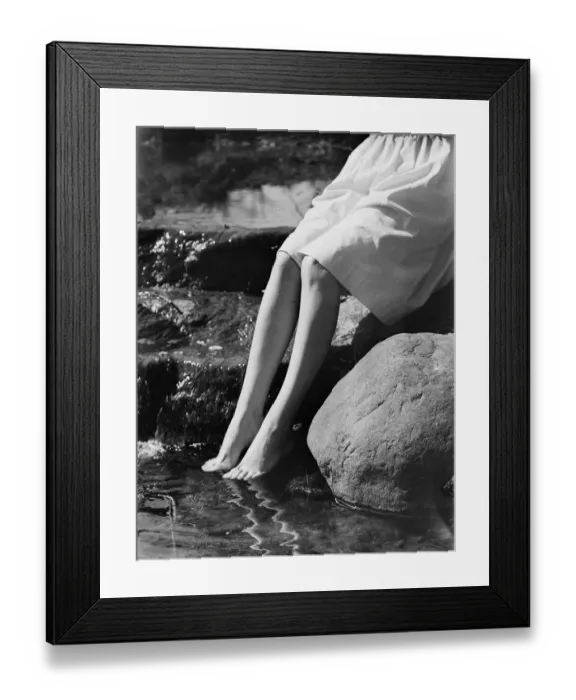 Framed Print : Woman sitting on rock with feet in water, low section