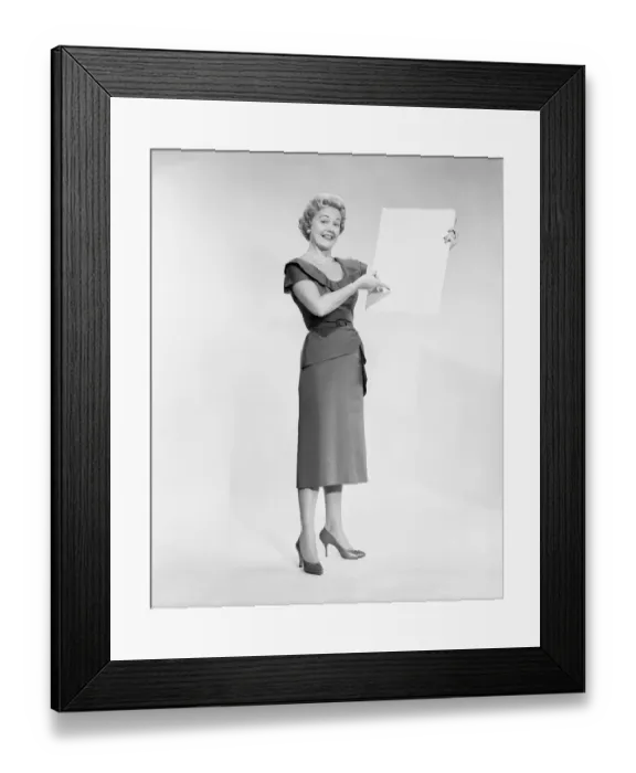 Framed Print : Woman holding blank piece of paper, portrait, studio shot Framed Print : Woman holding blank piece of paper, portrait, studio shot