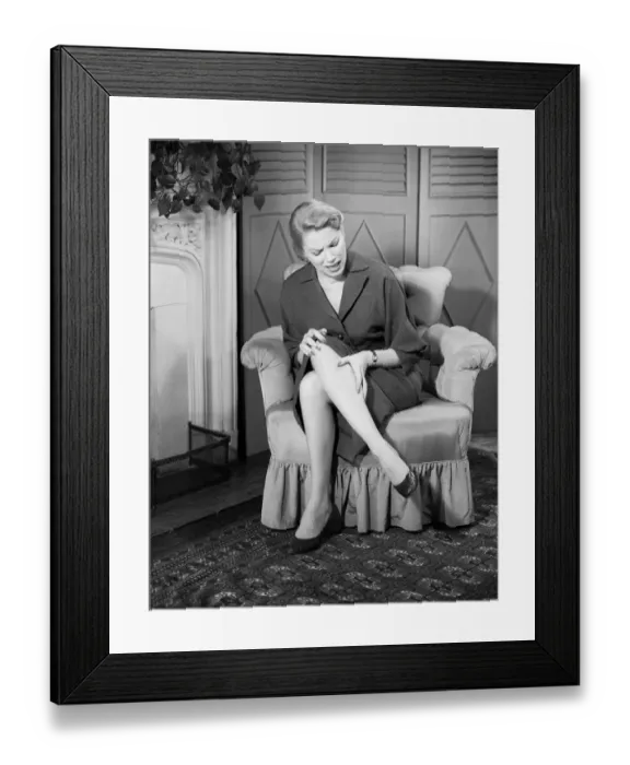 Framed Print : Woman rubbing leg in pain in living room Framed Print : Woman rubbing leg in pain in living room