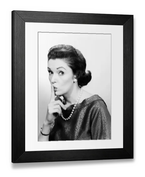 Framed Print : Studio portrait of mature woman holding finger to lips Framed Print : Studio portrait of mature woman holding finger to lips