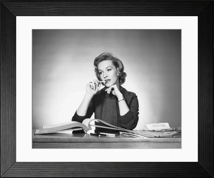 Framed Print : Woman chewing on pencil, book open in front of her Framed Print : Woman chewing on pencil, book open in front of her