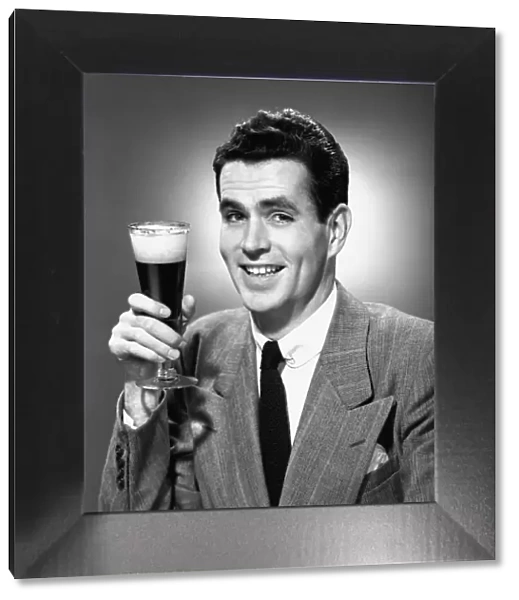 Man holding glass of beer in studio, (B&W), portrait
