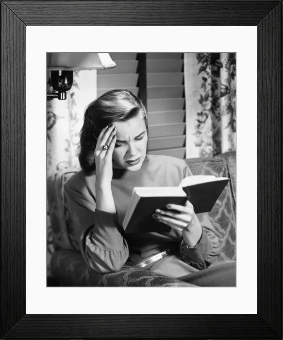 Framed Print : Woman reading book, touching forehead, (B&W) Framed Print : Woman reading book, touching forehead, (B&W)