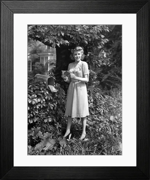 Framed Print : Woman standing at mailbox, holding letter, (B&W), portrait Framed Print : Woman standing at mailbox, holding letter, (B&W), portrait