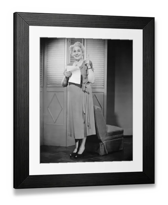 Framed Print : Senior woman holding sheet of paper, pointing up (B&W) Framed Print : Senior woman holding sheet of paper, pointing up (B&W)