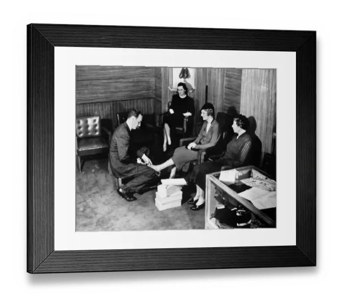Framed Print : Shop clerk measuring clients foot (B&W), elevated view Framed Print : Shop clerk measuring clients foot (B&W), elevated view