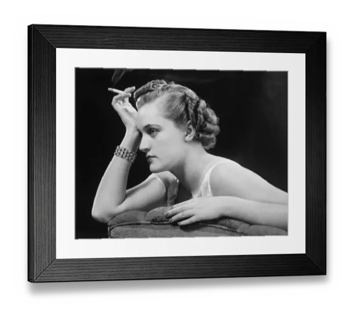 Framed Print : Glamourus woman sitting on sofa, holding cigarette (B&W) Framed Print : Glamourus woman sitting on sofa, holding cigarette (B&W)