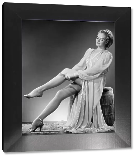 Young woman putting on stockings in studio (B&W)
