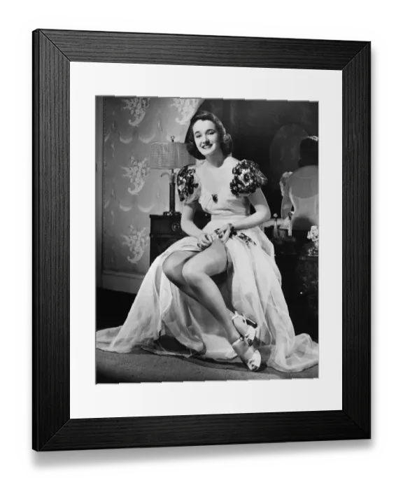 Framed Print : Woman in evening gown putting on stockings at vanity table (B&W), portrait Framed Print : Woman in evening gown putting on stockings at vanity table (B&W), portrait