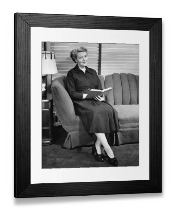 Framed Print : Senior woman sitting on sofa, holding book (B&W), portrait Framed Print : Senior woman sitting on sofa, holding book (B&W), portrait