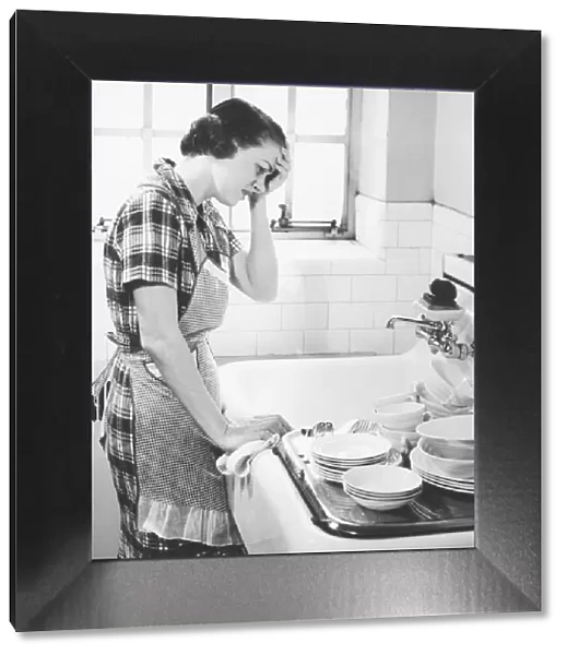Woman suffering headache standing at kitchen sink (B&W)
